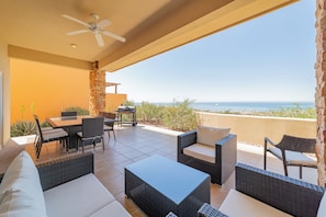 An outdoor patio with wicker furniture, a table, and chairs, overlooking a beach. - Puerta Cortés Colinas by Lumina (La Paz)