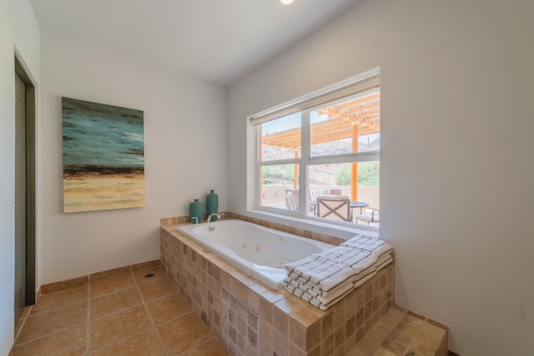Un baño con una bañera grande, una ventana que da al exterior y un cuadro en la pared.
