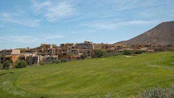 A residential area with multiple buildings, a green lawn, and a hilly backdrop.