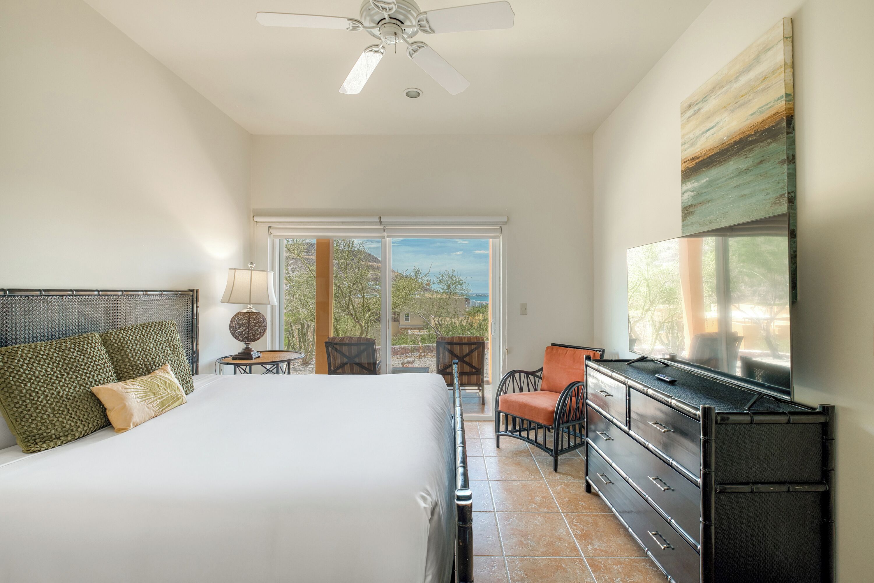 A bedroom with a bed, a TV, a dresser, a chair, and a balcony with a view.