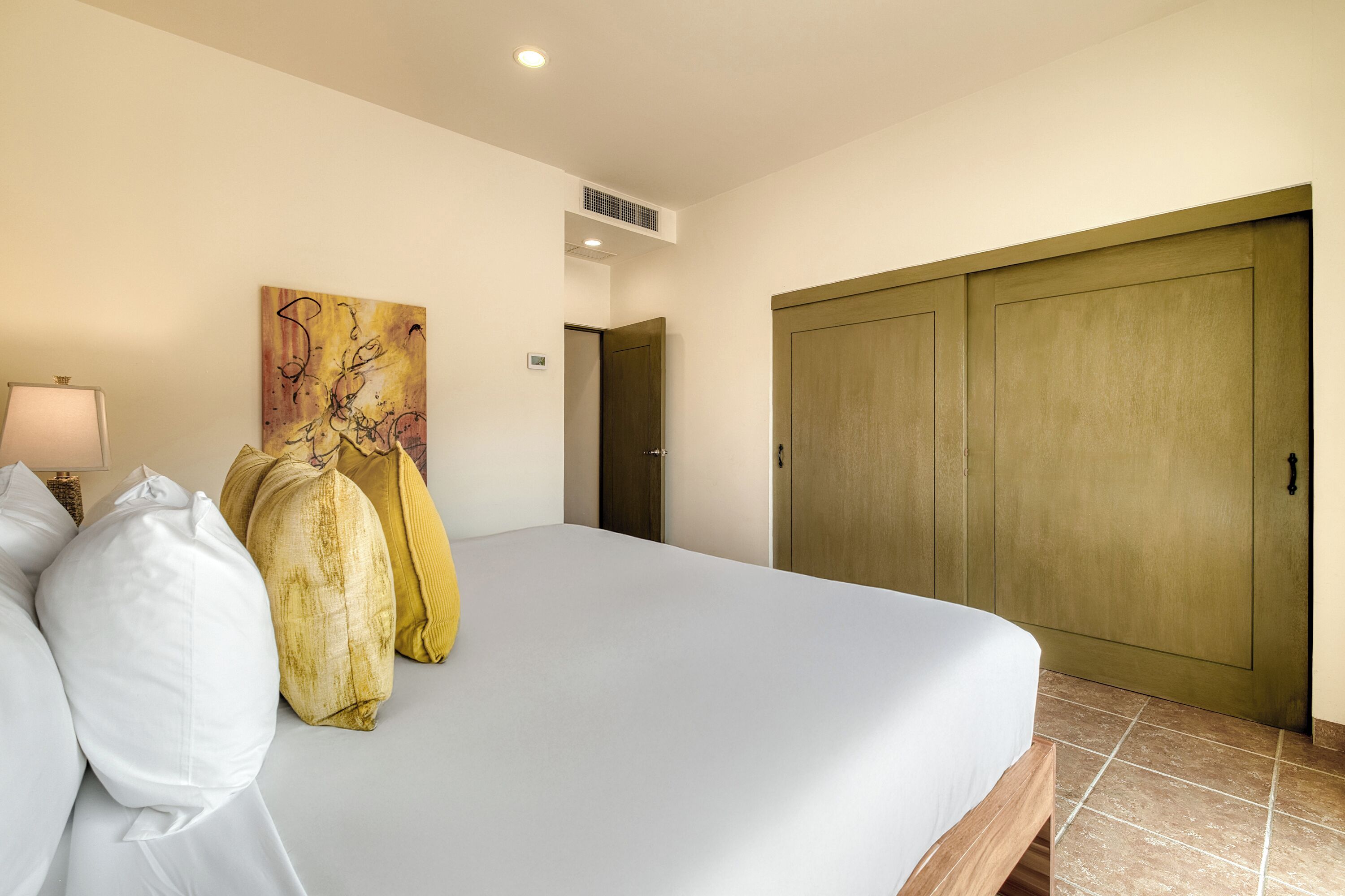 Une chambre d’hôtel avec un lit, un tableau, une lampe et une armoire.