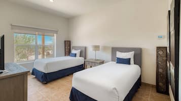 A hotel room with two beds, a desk, a lamp, and a window with a view of trees.