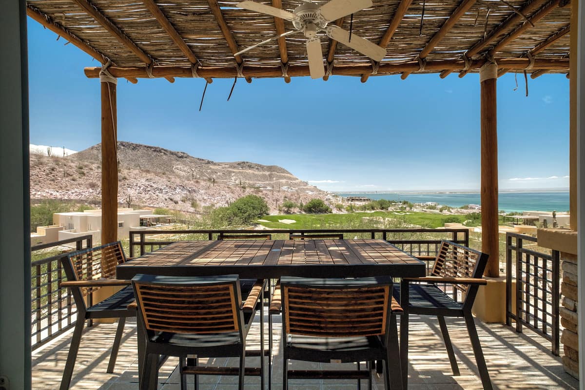 A covered outdoor seating area with a table and chairs, overlooking a golf course and the ocean.