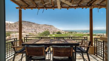 A covered outdoor seating area with a table and chairs, overlooking a golf course and the ocean.