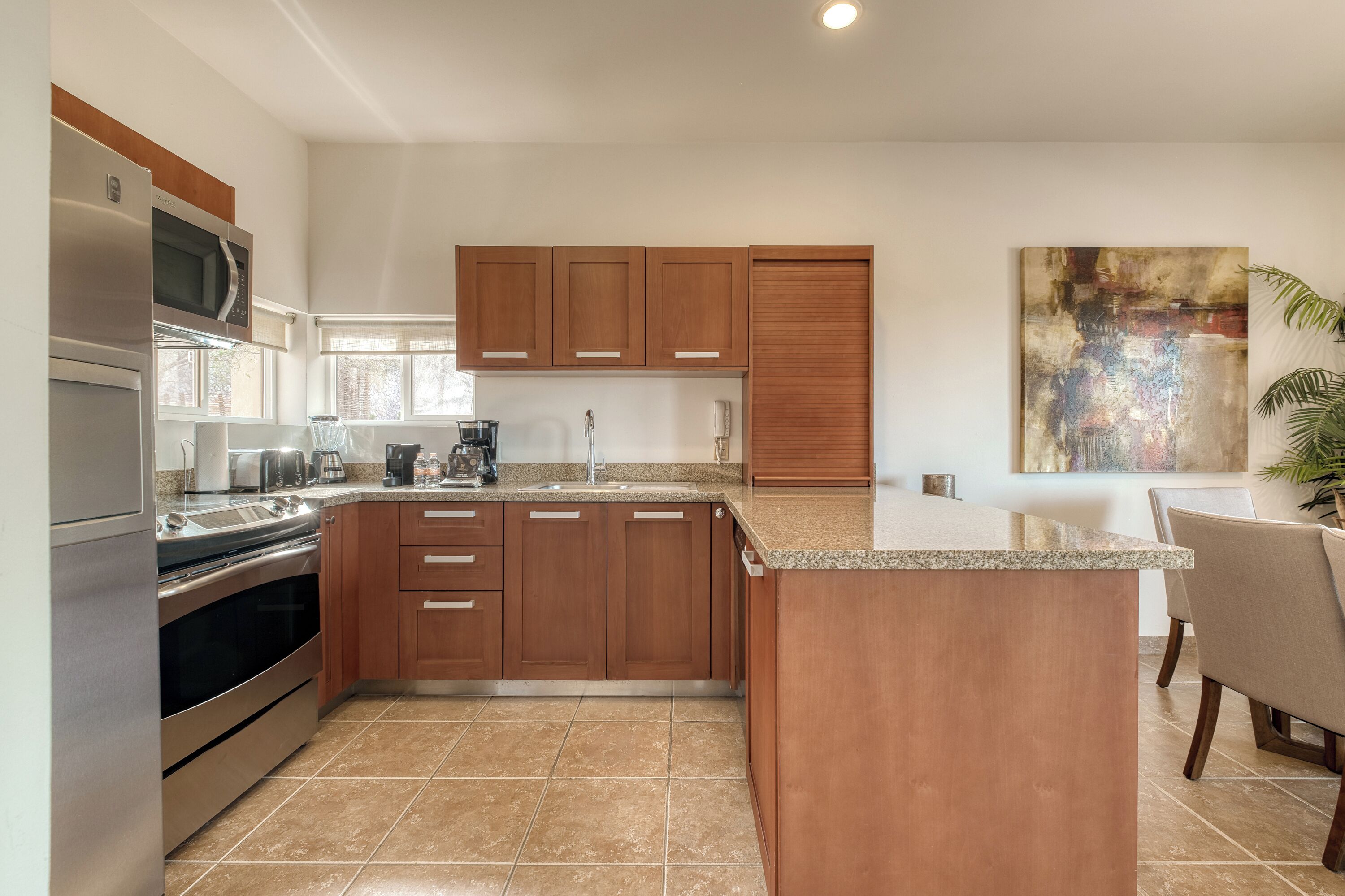 Una cocina moderna con una isla central, electrodomésticos de acero inoxidable, armarios de madera y un cuadro abstracto grande en la pared.