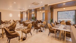 Un comedor moderno con varias mesas y sillas, ventanas amplias y un diseño de techo contemporáneo.