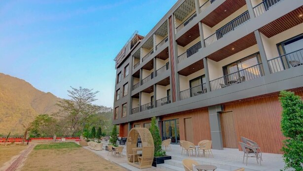 Un hotel de varios pisos con mesas al aire libre y vista a un paisaje montañoso.