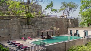 Una piscina con sillas de descanso y un pabellón, rodeada por un muro de piedra y vegetación.