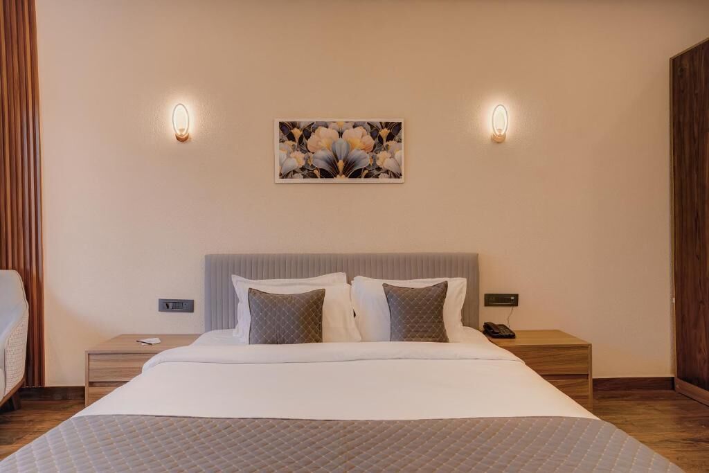 Habitación de hotel con cama, dos mesitas de noche, una lámpara de noche, un cuadro colgado en la pared y dos apliques de luz.