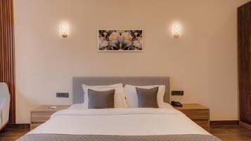 Habitación de hotel con cama, dos mesitas de noche, una lámpara de noche, un cuadro colgado en la pared y dos apliques de luz.