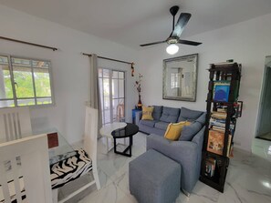 A living room with a sofa, ottoman, and a ceiling fan. - Villa Tropical - Penthouse 10 (Cabarete)