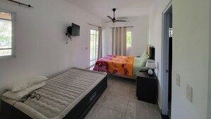 Ein Schlafzimmer mit einem Bett, einem Schreibtisch mit Lampe, einem Deckenventilator und einem an der Wand befestigten Fernseher.