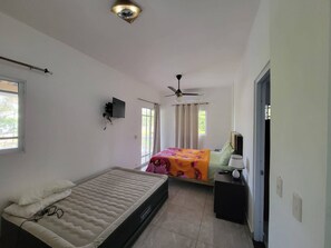 A bedroom with a bed, a desk with a lamp, a ceiling fan, and a TV mounted on the wall. - Villa Tropical - Penthouse 10 (Cabarete)