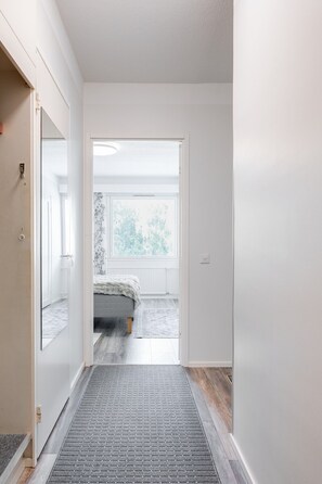A hallway leading to a bedroom with a bed, a window with a view, and a door on the left. - Pondside City Flat By Lapland Host (Rovaniemi)