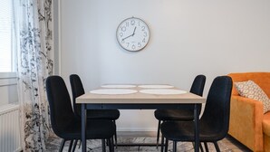 Ruokailutilassa on pöytä, neljä tuolia, seinällä oleva kello ja sohva.