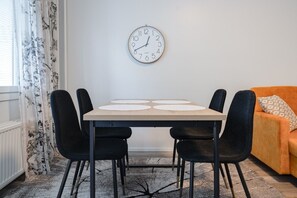 A dining area with a table, four chairs, a clock on the wall, and a sofa. - Pondside City Flat By Lapland Host (Rovaniemi)