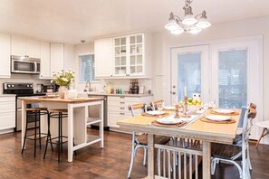 A modern kitchen with white cabinetry, a central island, bar stools, and a dining table set for six.