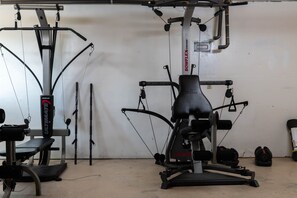 Une salle de sport équipée de matériel d’exercice, notamment un appareil Bowflex Ultimate, un banc et des haltères.
