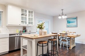 Une cuisine moderne avec des meubles blancs, un îlot central en bois, des tabourets de bar et une table à manger pour quatre personnes.