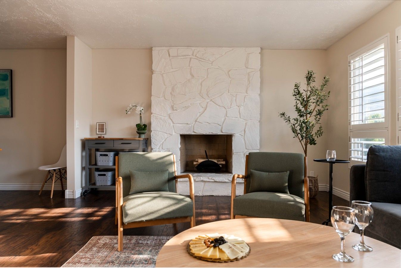 Una sala de estar con chimenea de piedra, dos sillones, una mesa de centro con una bandeja de quesos y una mesita con vasos.