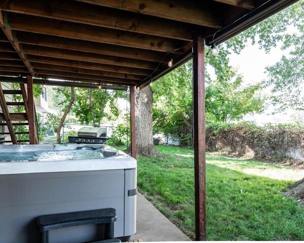 Un bain à remous sous une pergola en bois, avec une pelouse et des arbres en arrière-plan.
