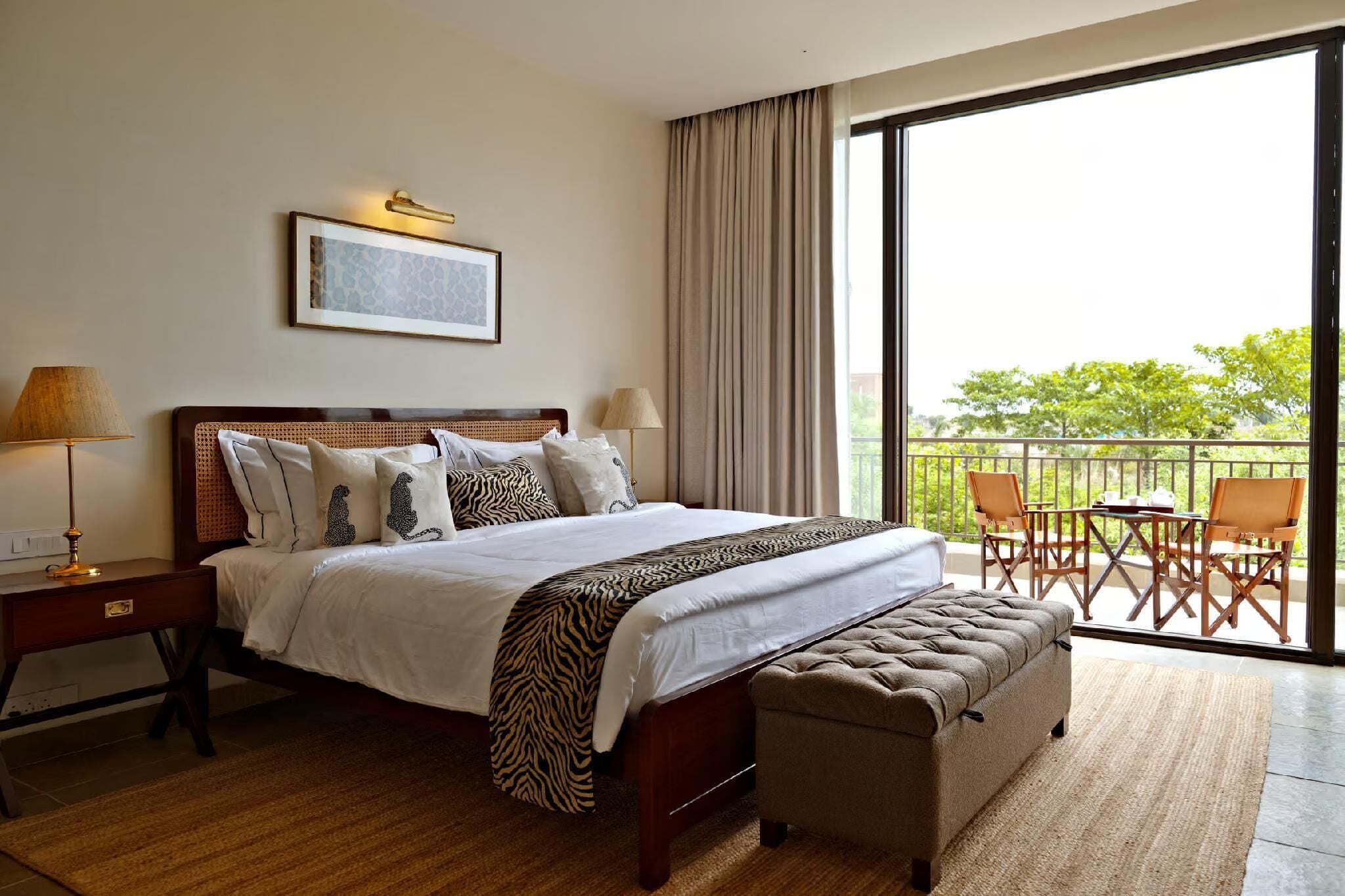 A hotel room with a large bed, a desk, a chair, and a balcony with outdoor furniture.