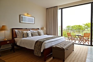 A hotel room with a large bed, a desk, a chair, and a balcony with outdoor furniture.