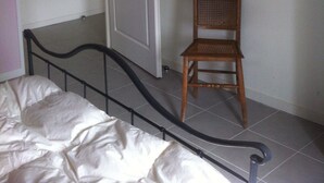 A bedroom with a bed, a chair, a door, and a tiled floor.