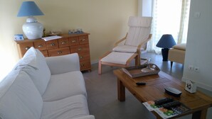 A living room with a sofa, a wooden coffee table with remote controls, a chair, a lamp, and a cabinet.