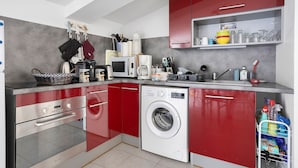 Cocina compacta con lavadora, microondas y armarios rojos.
