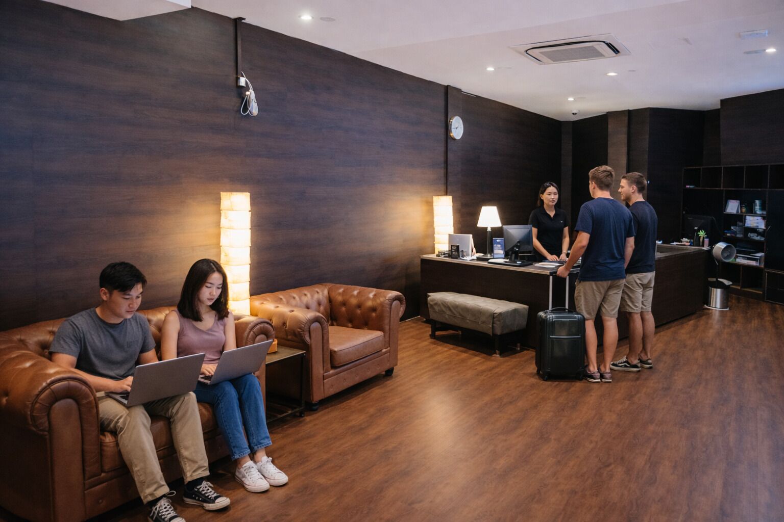 Een hotellobby met lederen banken, een receptiebalie en een bagagekar.