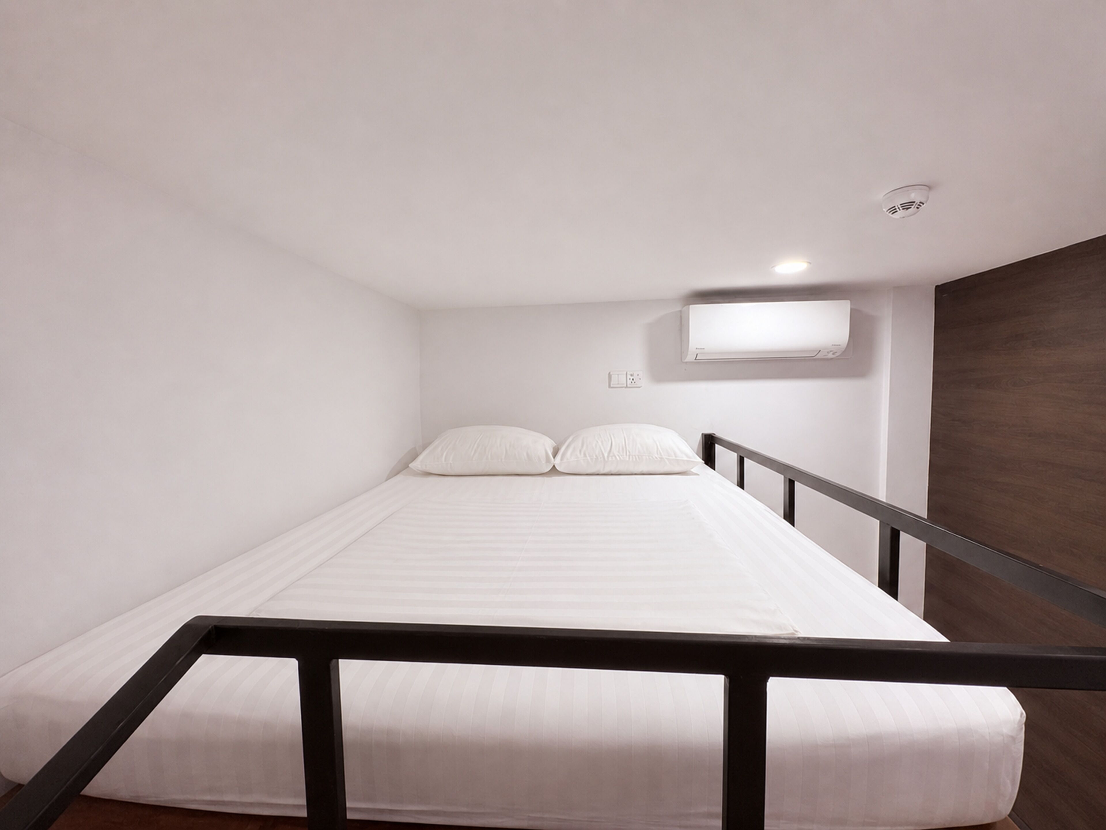 Een enkel bed met wit beddengoed, een zwart hoofdeinde, een witte muur en een houten paneel aan de rechterkant.