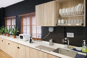 A modern kitchen with wooden cabinets, a microwave, a kettle, a sink, and a dish rack.