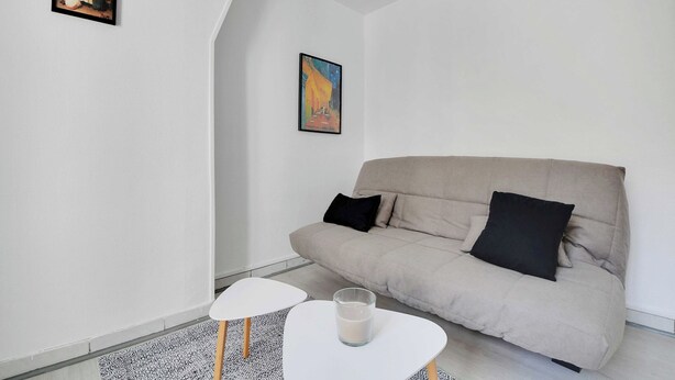 En minimalistisk stue med en beige sofa, to sorte puder, et hvidt sofabord med et glas mælk og et indrammet billede på væggen.