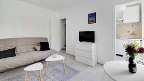 En moderne stue med sofa, fladskærms-tv, lille sofabord og en dekorativ vase.