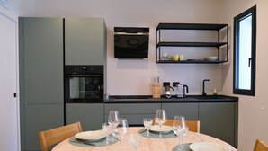 Eine moderne Küche mit grauen Schränken, einem eingebauten Backofen und einer schwarzen Arbeitsplatte. Ein Esstisch ist mit Tellern und Gläsern gedeckt.