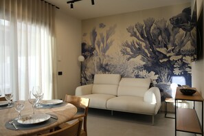 A dining area with a table set for four, a sofa, and a wall mural. - Bianco e Blu Boutique Apartments (Marina di Ragusa)