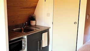 A compact kitchen with a sink, stove, and cabinets, a small potted plant, and a door with a coat hook.