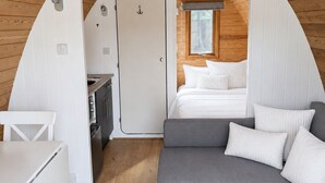 A compact, wooden interior with a kitchenette, a gray sofa, and a bed.