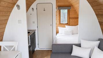 A compact, wooden interior with a kitchenette, a gray sofa, and a bed.