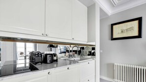 A modern kitchen with white cabinetry, a marble countertop, and a built-in sink. - Charming studio 2P - Musée d'Orsay / Louvre (Paris)
