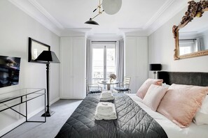 A hotel room with a bed, a TV, a desk, and a balcony view. - Charming studio 2P - Musée d'Orsay / Louvre (Paris)