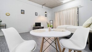A modern room with a round white table, two white chairs, a flat-screen TV, and a bed with white bedding.