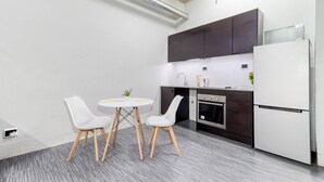 A modern kitchen with dark cabinets, a white refrigerator, and a small dining table with two chairs.