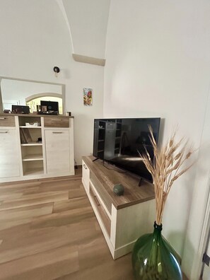 Ein modernes Wohnzimmer mit einem Flachbildfernseher, Holzschränken und einer Vase mit Trockenpflanzen.