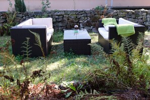 An outdoor seating area with wicker furniture and a stone wall in the background. - Atelier Schillerstraße – Spacious, Central Vacation Apartment in Eisenach (Eisenach)