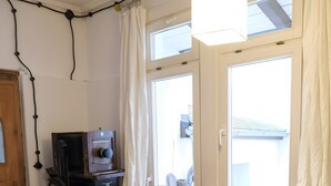 A room with a wooden floor, a red sofa, a small table with a device, and a window with curtains.