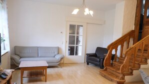 A living room with a sofa, a chair, a coffee table, and a wooden staircase.