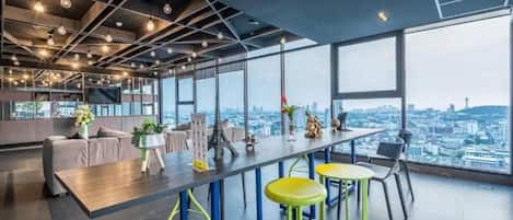 Um interior moderno com uma mesa comprida, banquetas de bar e grandes janelas com vista para a cidade.