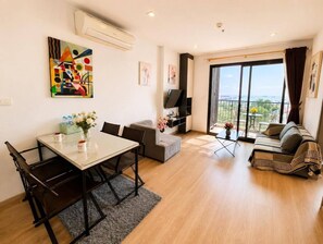 A modern living room with a dining area, a sofa set, a TV, and a large window with a view. - Sea View 2 Bed Room Best of Location (Pattaya)